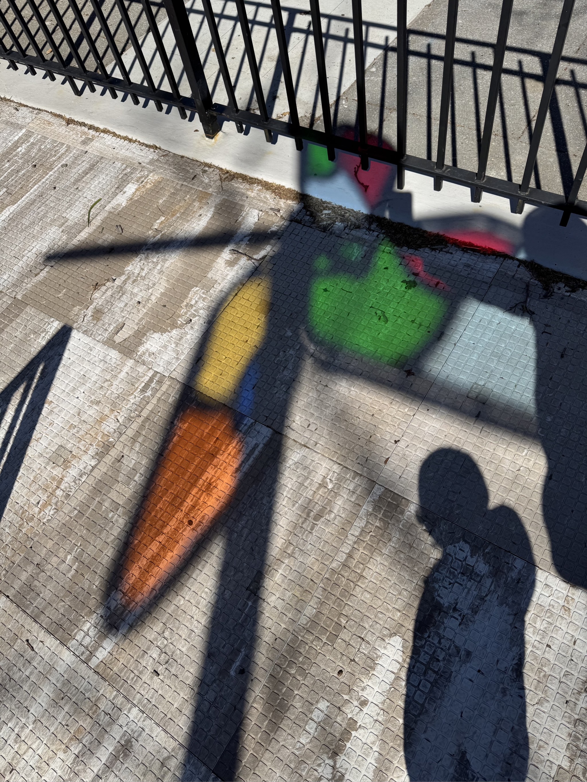 Colorful light reflections create rainbow patterns on textured concrete sidewalk.