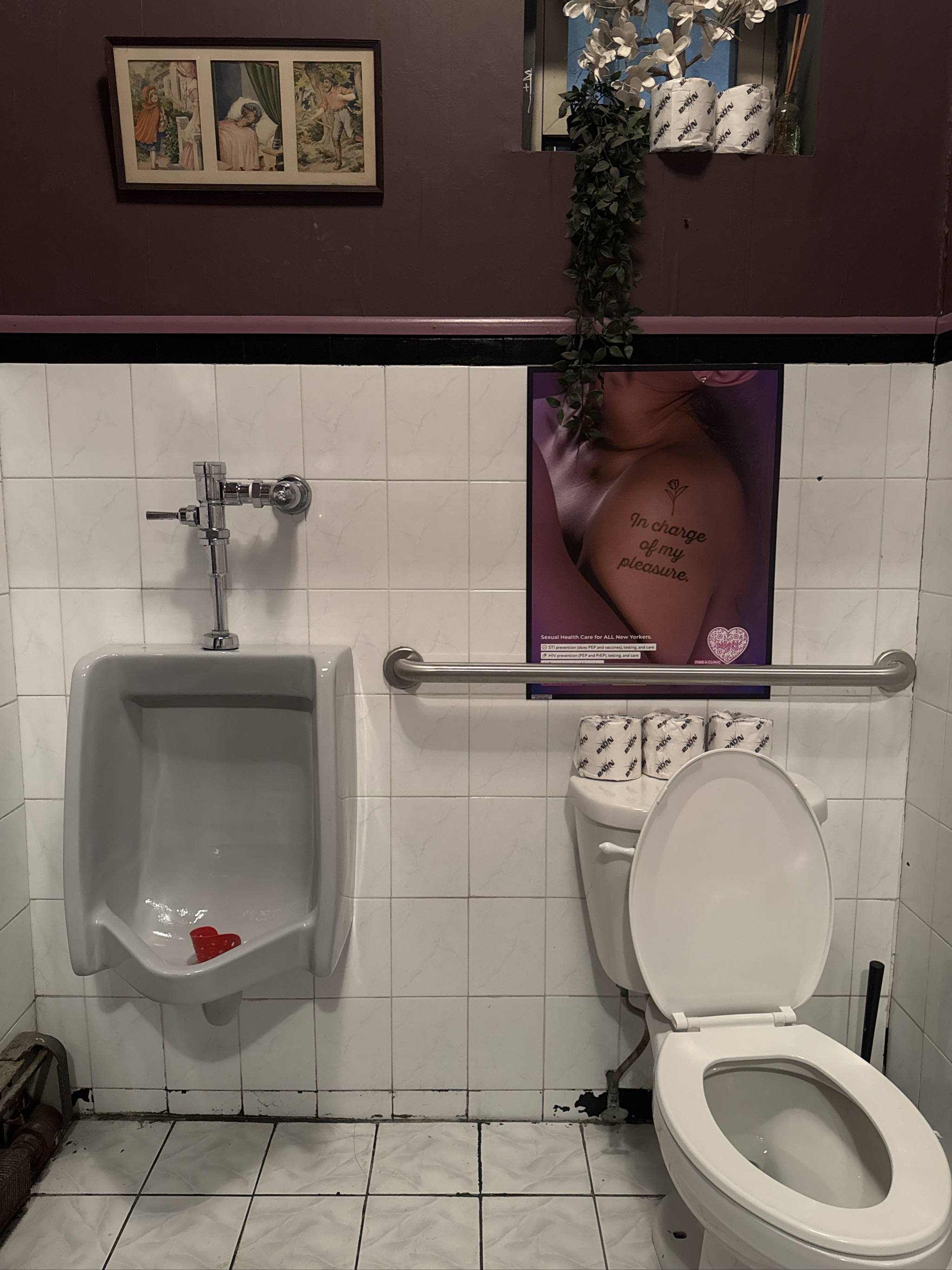 Bathroom with urinal, toilet, and provocative poster on wall.