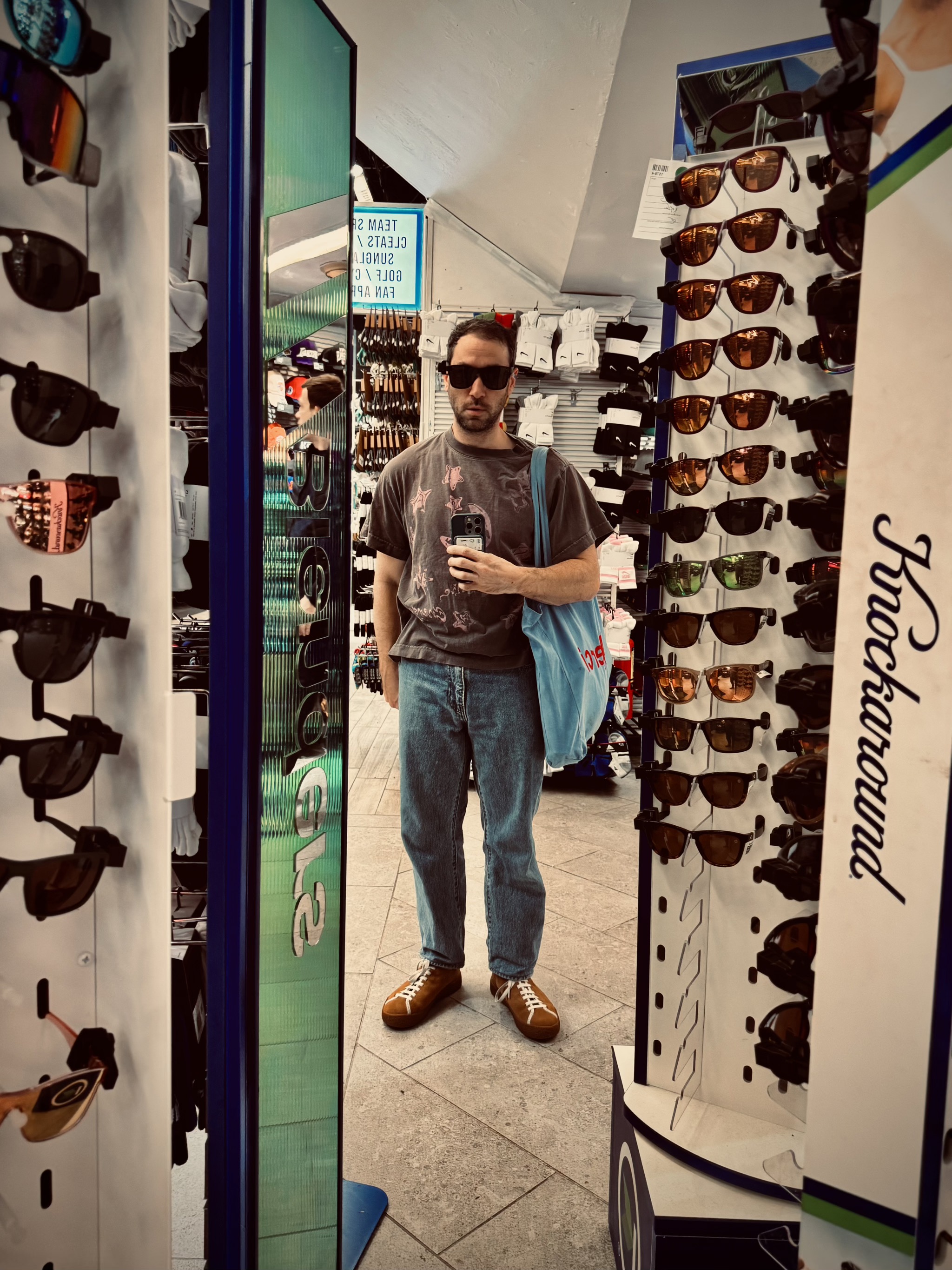 Man trying on sunglasses in a shop surrounded by displays.