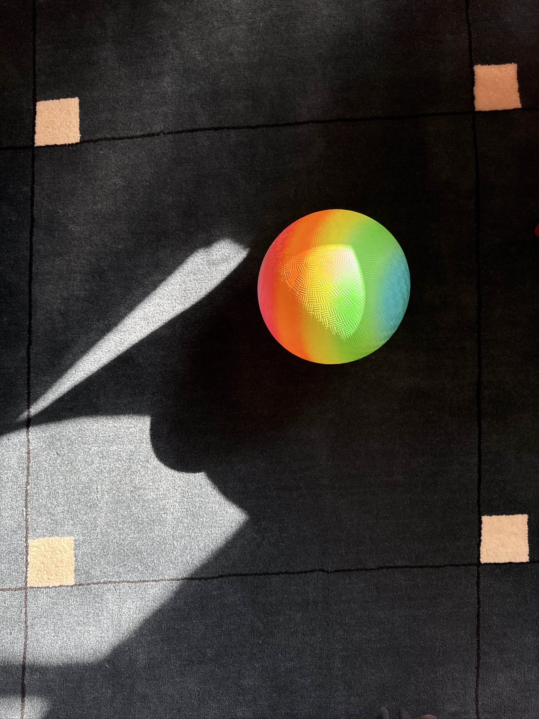 Colorful rainbow sphere on dark tiled floor with sunlight shadows.