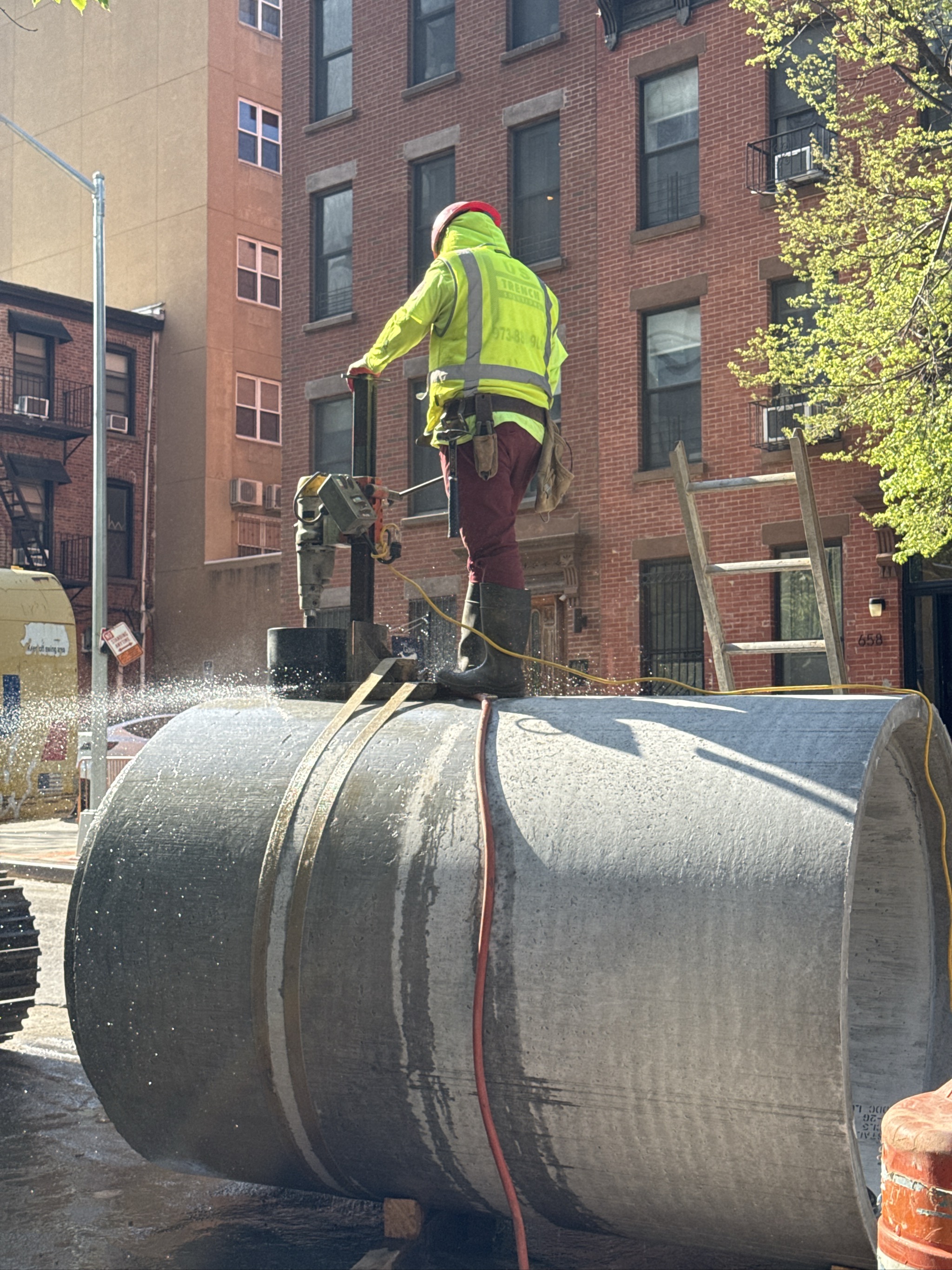 Construction worker cutting large concrete pipe with power saw