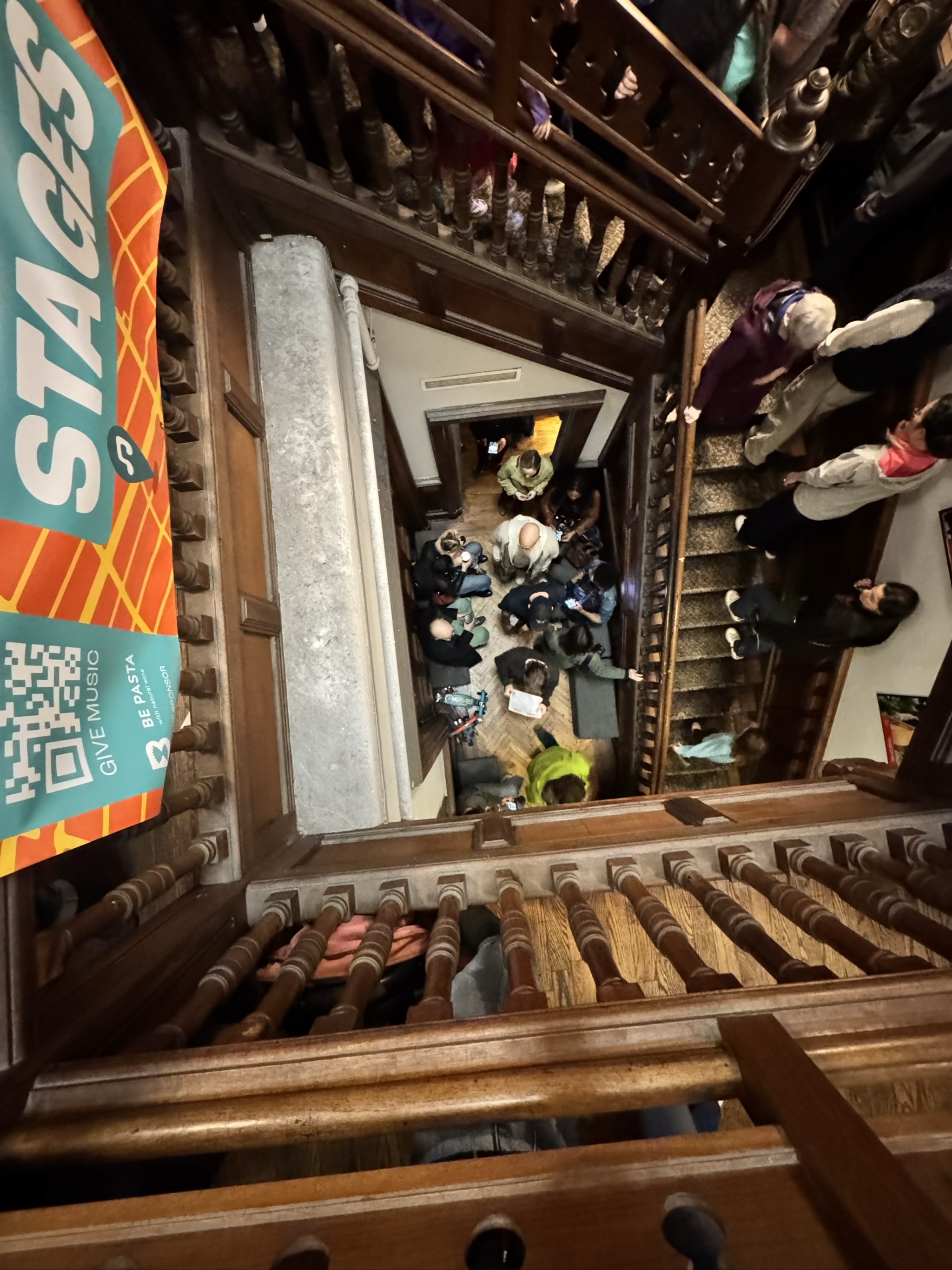 Looking down wooden staircase at crowded museum lobby below
