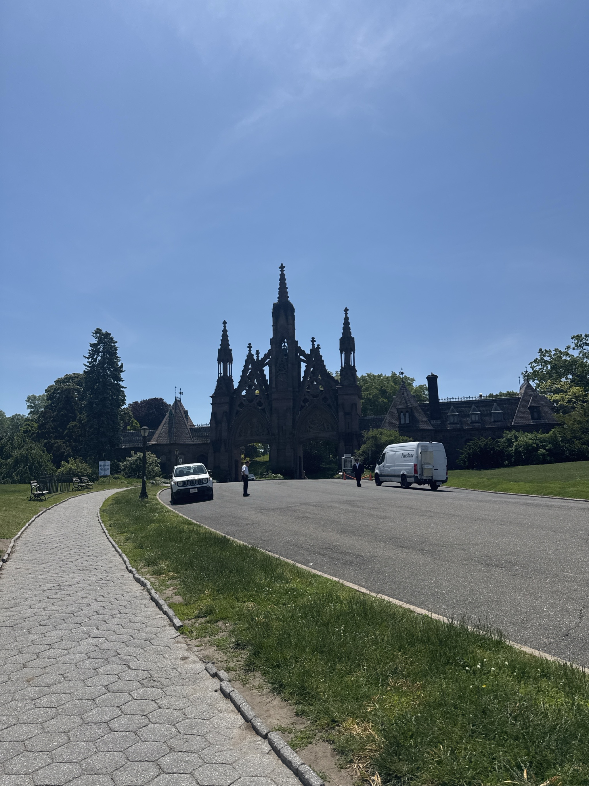 Gothic cathedral entrance with ornate spires beyond paved road and lawn.