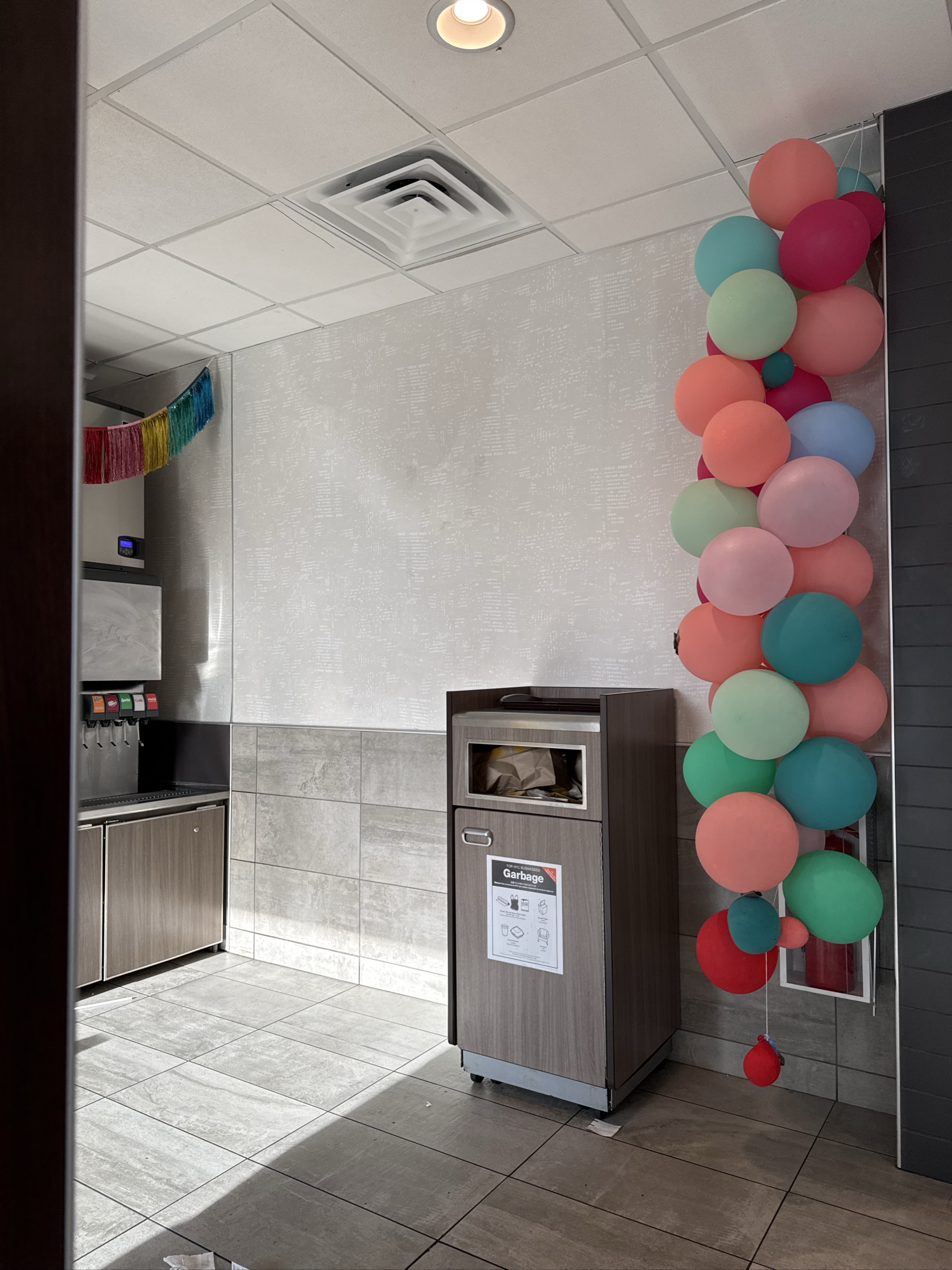 Colorful balloon garland decorates modern break room with garbage bin.