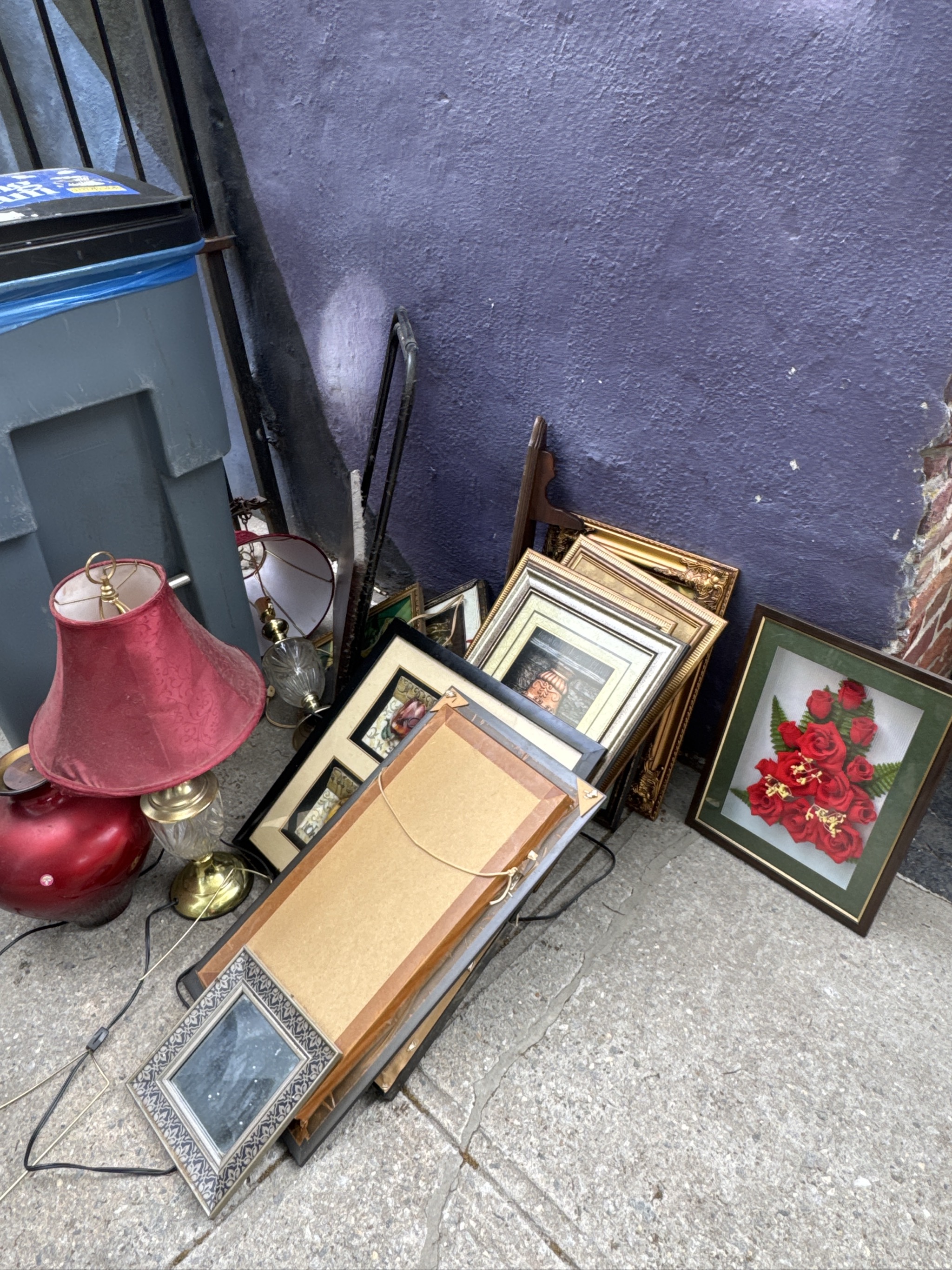 Various household items and framed pictures scattered on concrete pavement.