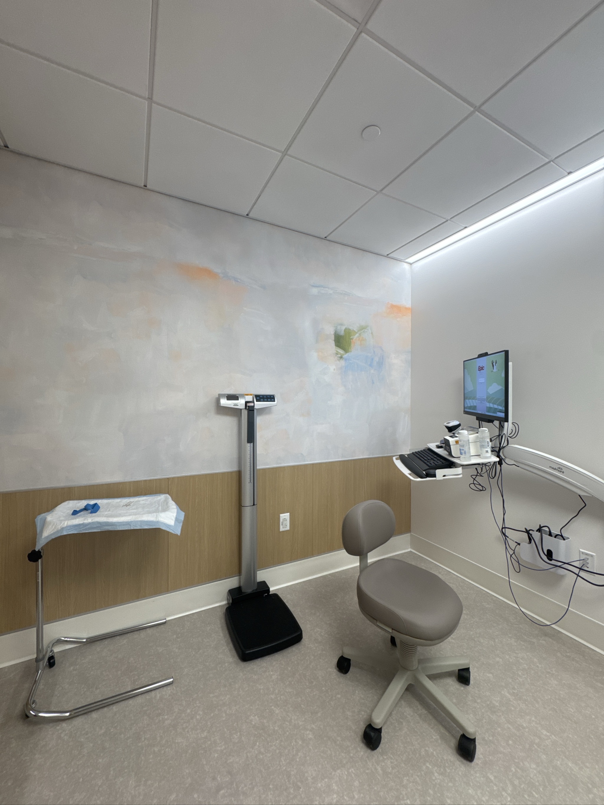 Medical examination room with scale, chair, and monitoring equipment.